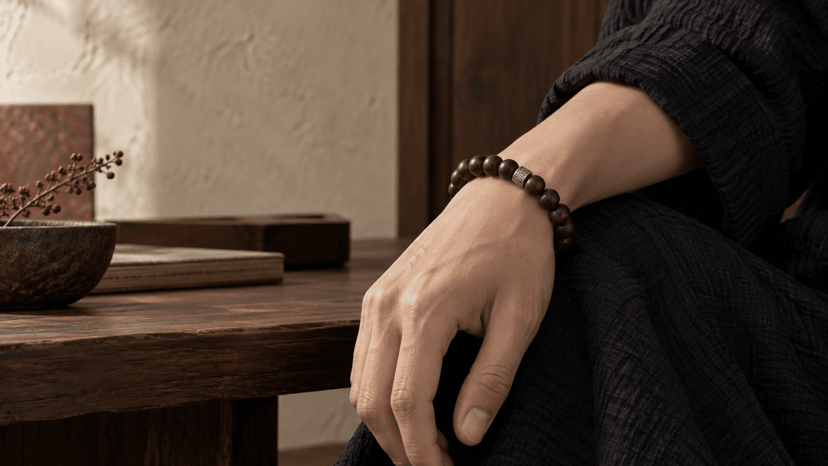 A dark agarwood bracelet worn against black cloth in a warm stone interior